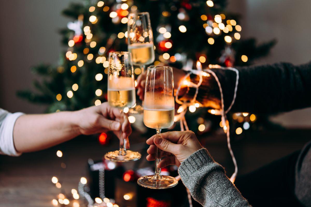 A group of hands clinking glasses of Champagne in front of a Christmas tree