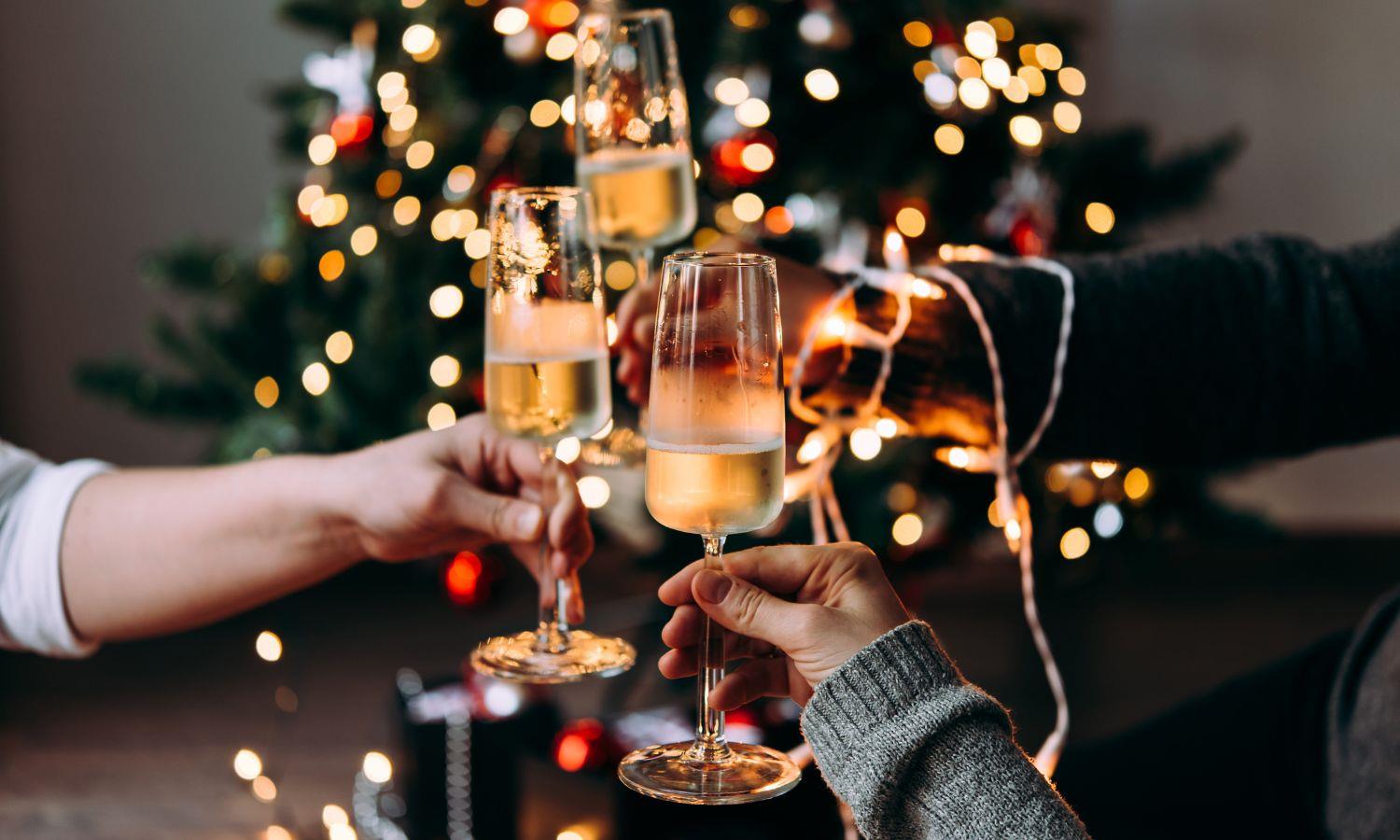 Three people holding Champagne glasses in front of a Christmas tree