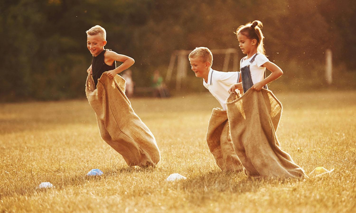 3 children doing a sack race on a sunny day